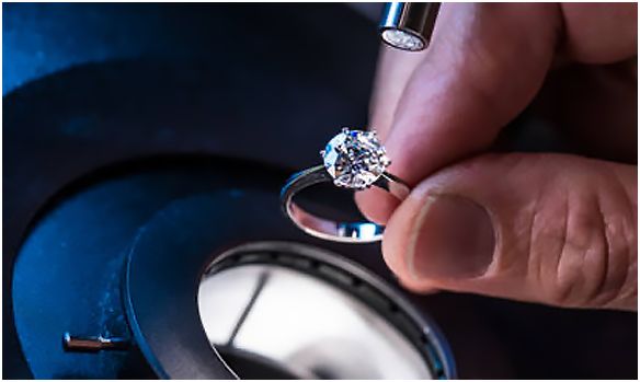 En person undersöker en diamantring med en lupp vid en värdering.